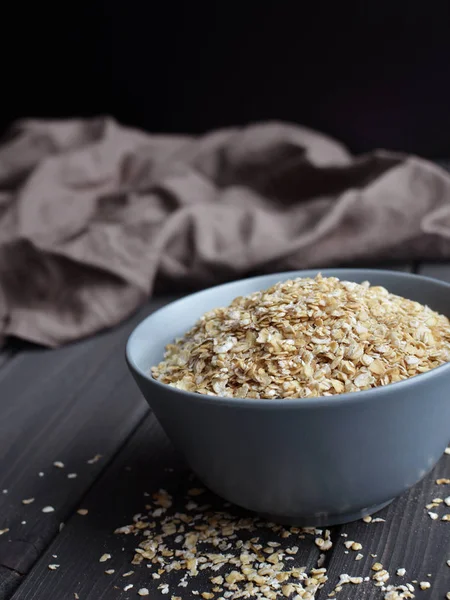 Rolled oats in ceramic bowl on dark wooden table with texture — Stock Photo, Image