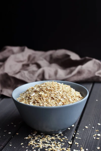Rolled oats in ceramic bowl on dark wooden table with texture — Stock Photo, Image