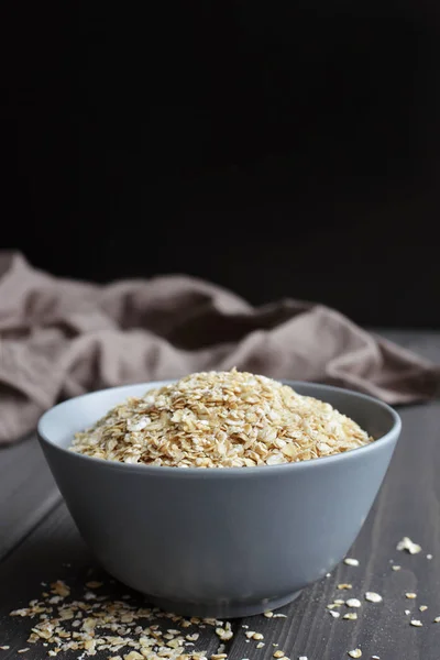 Rolled oats in ceramic bowl on dark wooden background, copy space — Stock Photo, Image