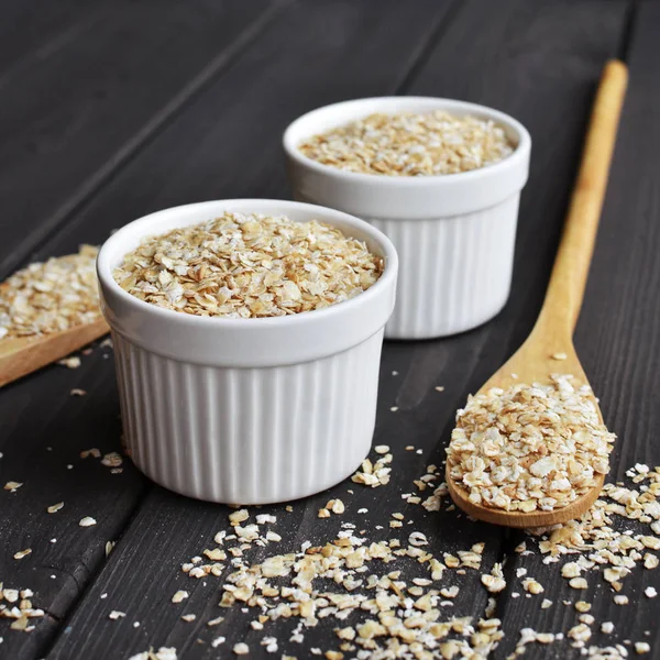 Avena laminada en cuencos y cucharas sobre fondo de mesa de madera oscura —  Fotos de Stock