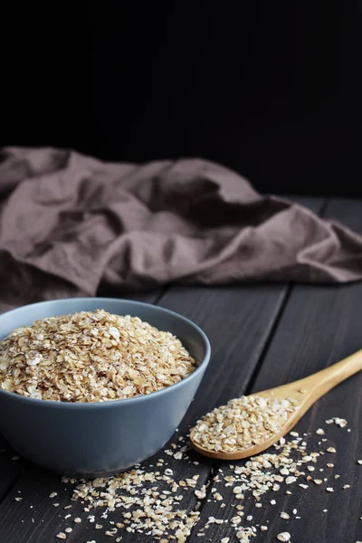 Rolled oats in bowl and spoon on dark wooden table background — Stock Photo, Image