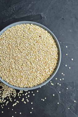 Seramik kasedeki kurumuş organik kinoa tohumları koyu beton arka plana saçılmış.