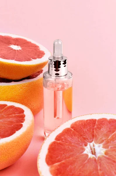 Bottle of grapefruit essential oil with fresh sliced grapefruits. Pink background. Aromatherapy treatment. Naturopathic medicine concept.
