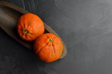 İki taze mandarin narenciye meyvesi, siyah grunge arka planda ahşap tabakta. Kış zamanı meyveleri. Üst görünüm, alanı kopyala.