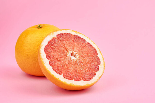 Fresh whole and cut red grapefruit citrus fruits on pink background, copy space