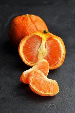 Siyah arka planda olgun, sulu mandalinalar. Yarım meyve, bütün bir tane ve dilimler. .