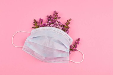 Pembe arka planda leylak çiçekleri olan cerrahi yüz maskesi.