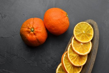 Taze mandalinalar ve kurutulmuş portakal dilimleri. Tahta tabakta, arka planda, üst tarafta.