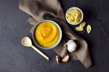 Koyu grunge arka planında taze sarımsak ve buğday ekmeği ile seramik bir kasede sonbahar balkabağı kremalı çorba. Geleneksel Şükran Günü yemeği. Üst görünüm