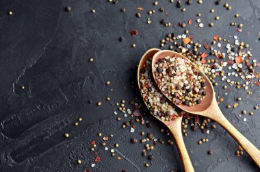 Çeşitli baharatlar koyu taşlı arka planda iki büyük tahta kaşıkta karıştırılır. Yemek pişirme konsepti. Üst görünüm, alanı kopyala