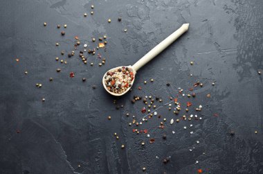 Deniz tuzu, farklı biber, kardamon, hardal tohumu ve ahşap kaşıkta kırmızı biber taneleri. Koyu grunge arka planda farklı baharatların karışımı. Üst Manzara. Boşluğu kopyala.