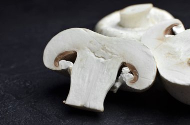 Şampiyon mantarları siyah taş arka planda ikiye bölünür. Vegan gıda konsepti. Yakın görünüm.