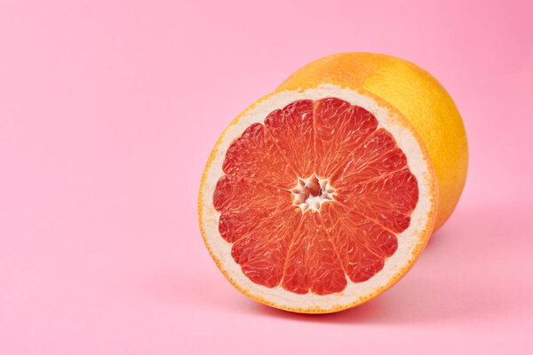 Whole and cut grapefruit citrus fruits on pink background, copy space