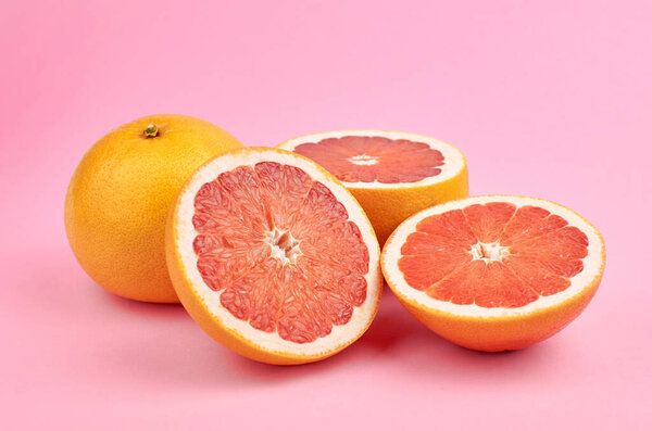 Lot of red grapefruit citrus fruits, whole and cut, over pink stylish background