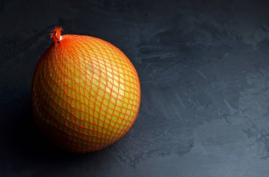Koyu gri arka planda koruyucu ağa sarılmış Pomelo meyvesi. Boşluğu kopyala.