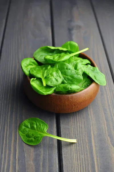 Fresh green spinach leaves in wooden bowl over old dark wooden table. Healthy vegan food. Green living and eco-conscious concept.