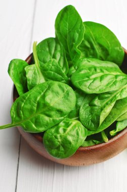 Beyaz ahşap arka planda koyu ahşap kâsede yeşil ıspanak yaprakları. Vegan gıda yaşam tarzı konsepti.