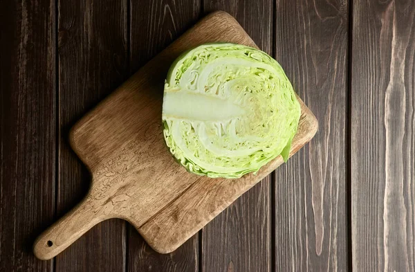 Half a head of fresh white cabbage on wooden cutting board over dark table background. — Stock Photo, Image