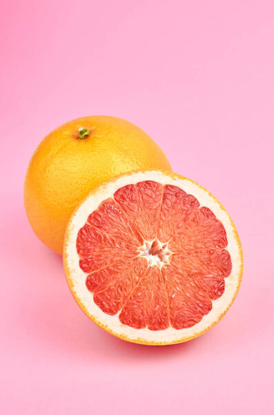 Whole and cut grapefruit citrus fruits on pink background