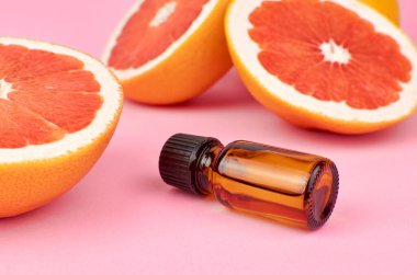 Pembe arka planda taze greyfurt parçaları olan saf greyfurt yağı. Güzellik ve sağlık hizmetleri kavramı.