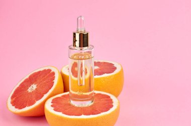 Cam şişedeki turunçgil yağı pembe arka planda taze ve sulu greyfurtlar, fotokopi alanı, doğal güzellik ve spa konsepti..