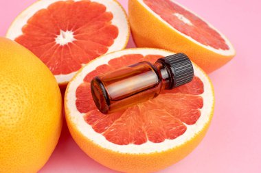 Pembe arka planda taze greyfurt parçaları olan saf greyfurt yağı. Güzellik ve sağlık hizmetleri kavramı.