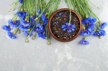 Kurumuş mısır çiçeği yapraklarıyla harmanlanmış bitki çayı ahşap kasede taze mısır çiçekleri gri arka planda, üst manzara, kopyalama alanı