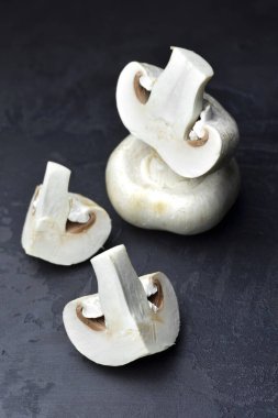 Çiğ şampiyon mantarlar, kesilmiş ve tamamı koyu gri renkli arka plan. Vejeteryan yemek pişirme.