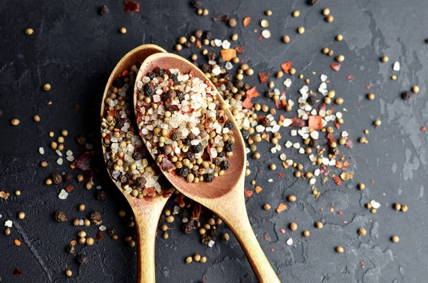 Les épices multicolores se mélangent dans des cuillères en bois sur fond sombre - poivrons, sel de mer, cardamon, graines de moutarde et flocons de paprika. Les ingrédients alimentaires. — Photo