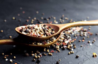 Koyu arkaplanda çok renkli baharatlı kaşıklar - biber karışımı, deniz tuzu, kardamon, hardal tohumu ve kırmızı biber taneleri.