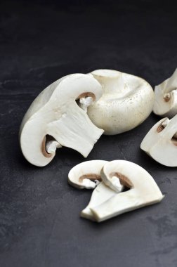 Koyu arkaplanda taze şampiyon mantarları, dilimlenmiş ve bütün, pişirmeye hazır..