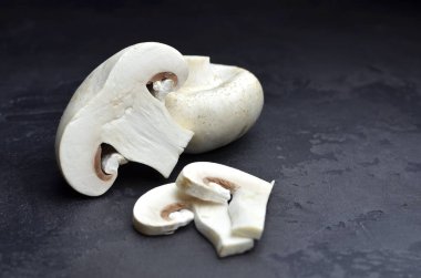 Çiğ şampiyon mantarlar, kesilmiş ve tamamı koyu gri masa arkaplanı. Vejeteryan yemek pişirme. Boşluğu kopyala.