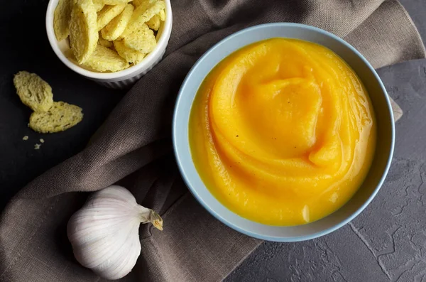 Butternut squash soup with croutons and fresh garlic in ceramic bowl with metal spoon on grunge black background with linen napkin. Top view — Stock Image Butternut Squash Soup Croutons Fresh Garlic Ceramic Bowl Metal Spoon Royalty Free Stock Images