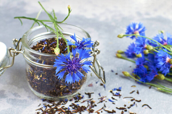 Black tea mix with dried cornflower petals and thyme in glass jar with fresh cornflowers.