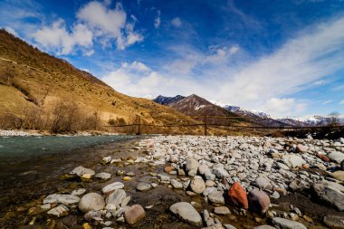 Dağ nehir kaya ve kayalık ve karla kaplı dağlar arka plan üzerinde asma köprü ile hızlı akışı ile. Gürcü askeri yola manzara.