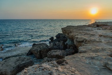 Kıbrıs Rum Kesimi 'nin Ayia Napa kenti yakınlarındaki Cape Greco' da gün batımında deniz mağaraları olan kayaların manzarası.