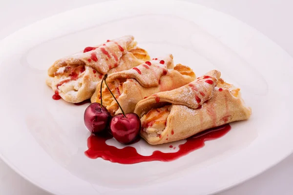 Pies with cottage cheese and powdered sugar on a white background. Traditional Russian pastry dish with cherry berries and syrup.