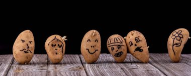 Ahşap bir masada ve siyah bir arka planda yüzü boyanmış komik bir patates. Yemek pişirmek için masada taze patates var..