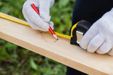 İş eldivenli bir marangoz, tahta üzerinde iz bırakmak için kalem ve bant mezurası kullanır. İnşaat endüstrisi, marangozluk atölyesi.