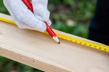 İş eldivenli bir marangoz, tahta üzerinde iz bırakmak için kalem ve bant mezurası kullanır. İnşaat endüstrisi, marangozluk atölyesi.