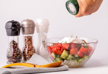 Bir kadın sebze salatasına baharat katar. Masanın üzerinde bir tabak salata, bir kaşık ve çeşitli baharatlar var. Sağlıklı ve sağlıklı yemek pişirme kavramı.