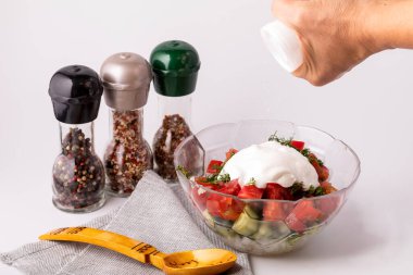 Bir kadın sebze salatasını tuzlar. Masanın üzerinde bir tabak salata, bir kaşık ve çeşitli baharatlar var. Sağlıklı ve sağlıklı yemek pişirme kavramı.