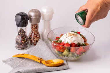 Bir kadın sebze salatasına baharat katar. Masanın üzerinde bir tabak salata, bir kaşık ve çeşitli baharatlar var. Sağlıklı ve sağlıklı yemek pişirme kavramı.