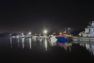 Gece manzarası, park yeri manzaralı bir sürü gemi ve tekne. Projektörler tekne istasyonunu aydınlatıyor.