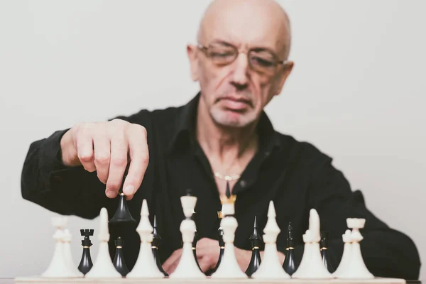 Senior man making move at chess game (focus on the hand holding chess piece)