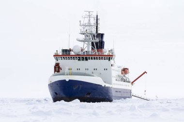 Research icebreaker docked over an ice floe in Antarctica clipart