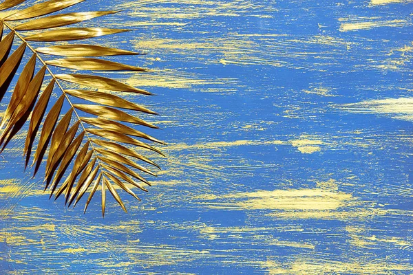 a golden palm branch on a decorative painted blue background with golden smears