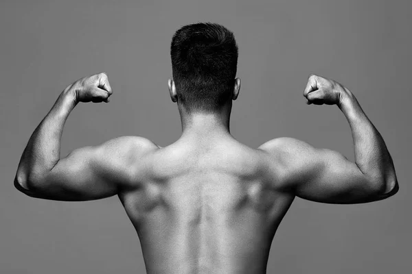 Black-and-white, monochrome photo - man with muscular body and strong back of bodybuilder athlete with biceps and triceps on grey background, sport and training — Stock Photo, Image