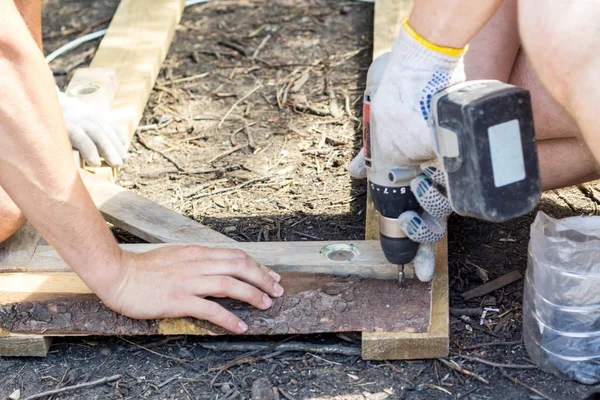 Close up of hands of a carpenter worker screws a bolt in a wooden board with a screwdriver on construction site.