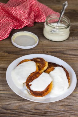 Süzme peynir ile Pancakes, ekşi krema beyaz bir tabak içinde.